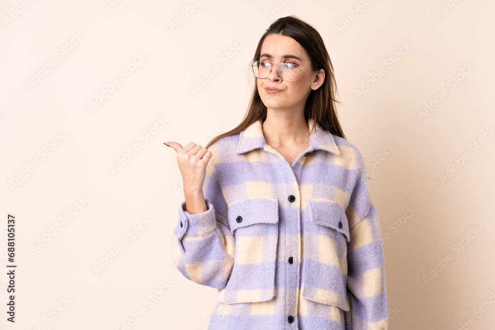 Young woman over isolated beige background unhappy and pointing to the side Young woman over isolated beige background unhappy and pointing to the side