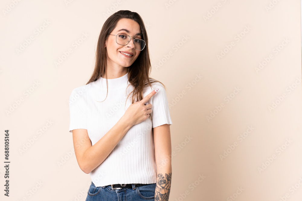 Young woman over isolated beige background pointing to the side to present a product