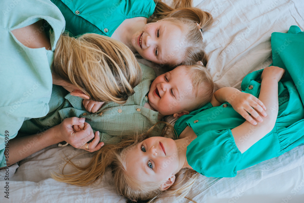 Top view of the children lying on the bed playing with their mother, two sisters and a baby brother spending time with their mother at home. Motherhood, childhood. Happy family at home.