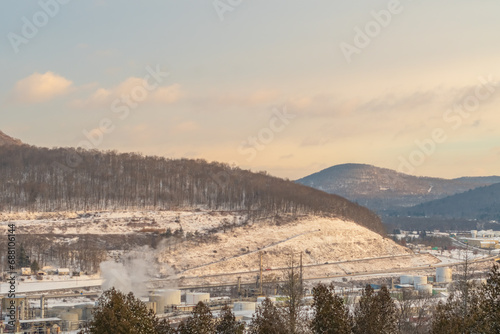 Bradford Pennsylvania, USA: November 29 2023 Oil refinery during winter snowy morning rising sunlight, historic cementary overlooking the town of bradford, oil refinery