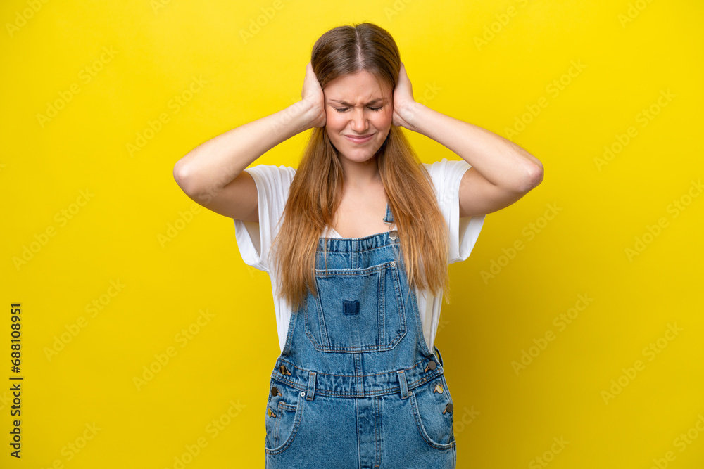 Young caucasian woman isolated on yellow background frustrated and covering ears