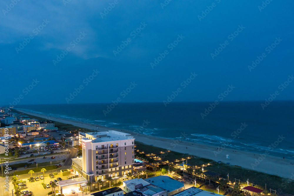 an aerial shot along the coastline of the Atlantic ocean with blue water, a sandy beach, hotels and condominiums and cars on the street at night with lights in Carolina Beach North Carolina USA