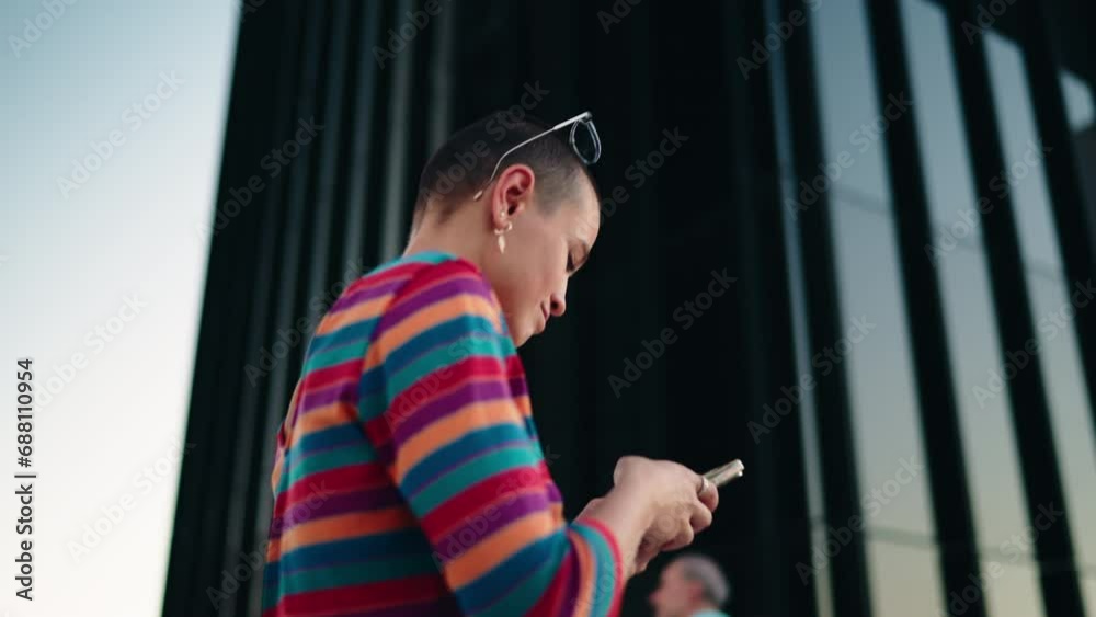 Millennial female walks in city and engaging in lively chatting through mobile phone app. Attractive laughing young woman sending text message to friends while holding smartphone device in hands Millennial female walks in city and engaging in lively chatting through mobile phone app. Attractive laughing young woman sending text message to friends while holding smartphone device in hands
