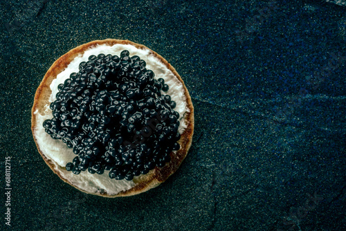 A blini with caviar and cream cheese, shot from above on a black slate background with copy space photo