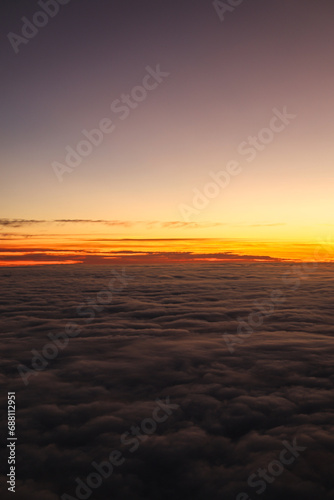 Sunset over the clouds. Beautiful orange color sky over a sea of clouds, view from the airplane window. Flying through the clouds, amazing nature landscape.