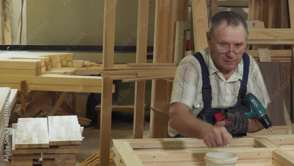 Carpenter Uses Electric Screwdriver Instrument To Pierce Wood With Screw. Wood Carpenter Manually Works With Power Instrument In Workshop. Carpenter Producing Wooden Window Frame With Instrument Carpenter Uses Electric Screwdriver Instrument To Pierce Wood With Screw. Wood Carpenter Manually Works With Power Instrument In Workshop. Carpenter Producing Wooden Window Frame With Instrument