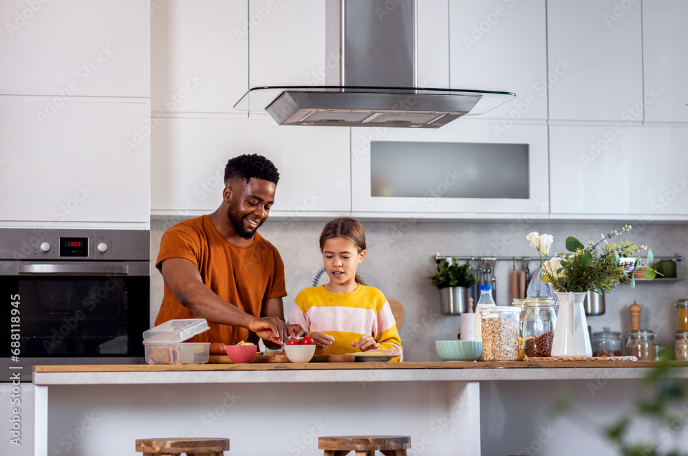 Smiling young single father with his daughter preparing lunch for school in the kitchen at home. Smiling young single father with his daughter preparing lunch for school in the kitchen at home.