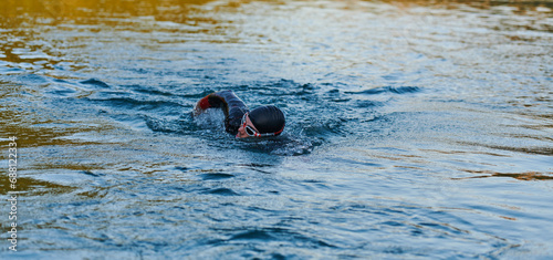 Triathlon athlete swimming on lake in sunrise wearing wetsuit