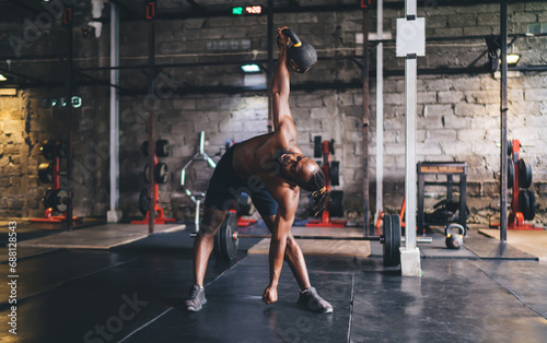 Fit young athlete doing windmill exercise with kettlebell in gym