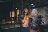 Powerful African American male athlete doing single kettlebell exercise in gym