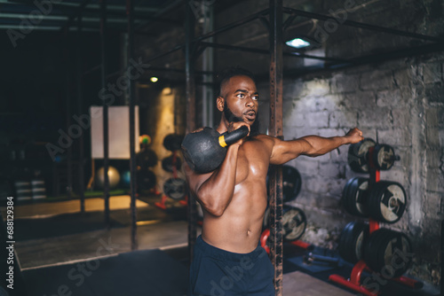 Powerful African American male athlete doing single kettlebell exercise in gym