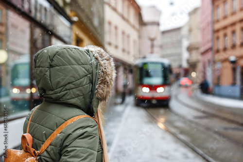 Public transport in the city during snowfall. Woman with winter coat is waiting for tram on street