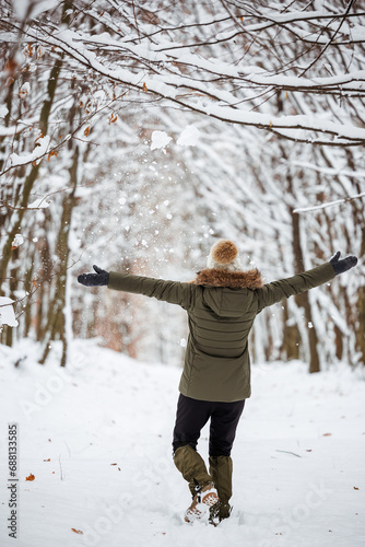 Happy woman enjoying walking in snow at winter forest. Warm clothing for leisure activity in cold weather