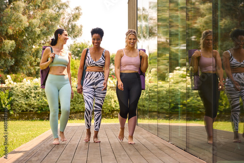 Three Mature Female Friends Outdoors In Fitness Clothing Carrying Exercise Mats At Gym Or Yoga Class photo