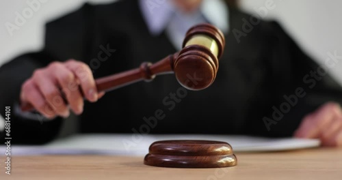 Female judge in robe hits court gavel on wooden surface photo