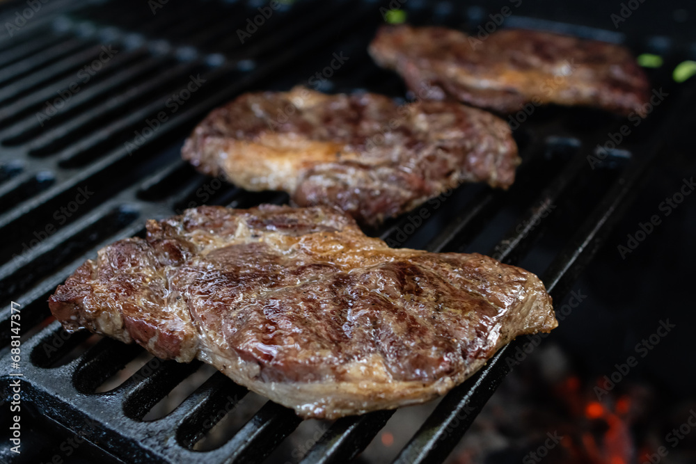 Three ribeye steaks are cooked on a charcoal grill on a cast iron grate