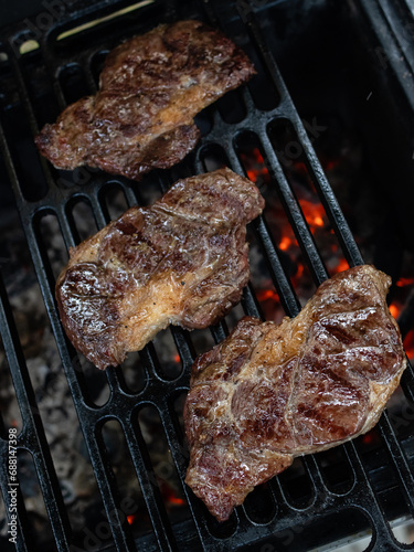 Three ribeye steaks are cooked on a charcoal grill on a cast iron grate