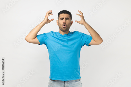 Portrait of shocked tired exhausted unshaven man wearing blue T- shirt standing showing mind blowing gesture, having annoyed and nervous expression. Indoor studio shot isolated on gray background. photo