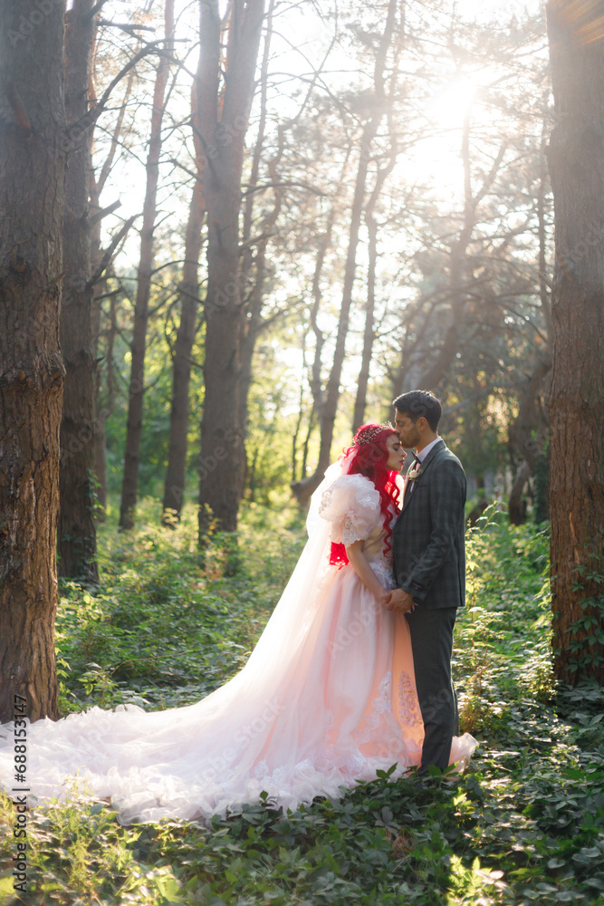 Beautiful couple, the groom in a green suit and the bride in an unusual pink wedding dress, posing at a luxurious ceremony with beautiful decor and an arch with a chandelier and candles in the forest Beautiful couple, the groom in a green suit and the bride in an unusual pink wedding dress, posing at a luxurious ceremony with beautiful decor and an arch with a chandelier and candles in the forest