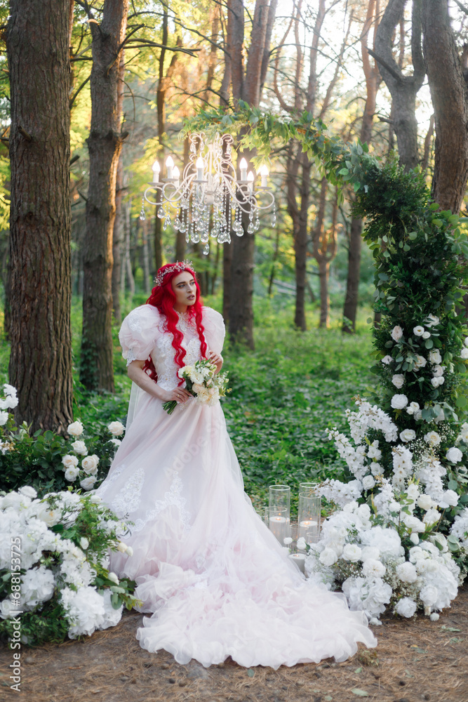 Beautiful couple, the groom in a green suit and the bride in an unusual pink wedding dress, posing at a luxurious ceremony with beautiful decor and an arch with a chandelier and candles in the forest Beautiful couple, the groom in a green suit and the bride in an unusual pink wedding dress, posing at a luxurious ceremony with beautiful decor and an arch with a chandelier and candles in the forest