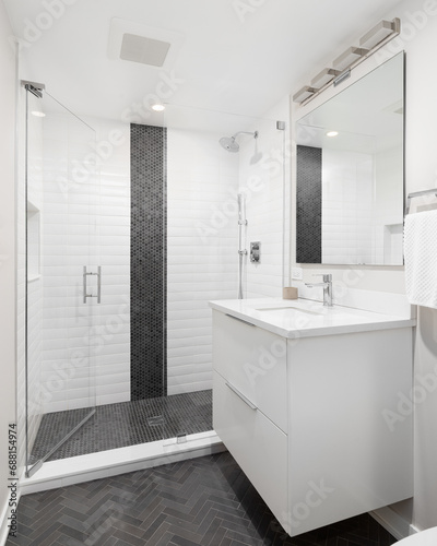 A bathroom with a white cabinet, charcoal herringbone tile floor, and a shower with white subway and black circular tiles.
