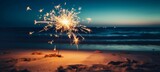 Sylvester New Year, Vacation holiday New Year's Eve 2024 party event celebration holiday greeting card - Closeup of sparkling sparkler stuck in sand on beach with ocean in teh background