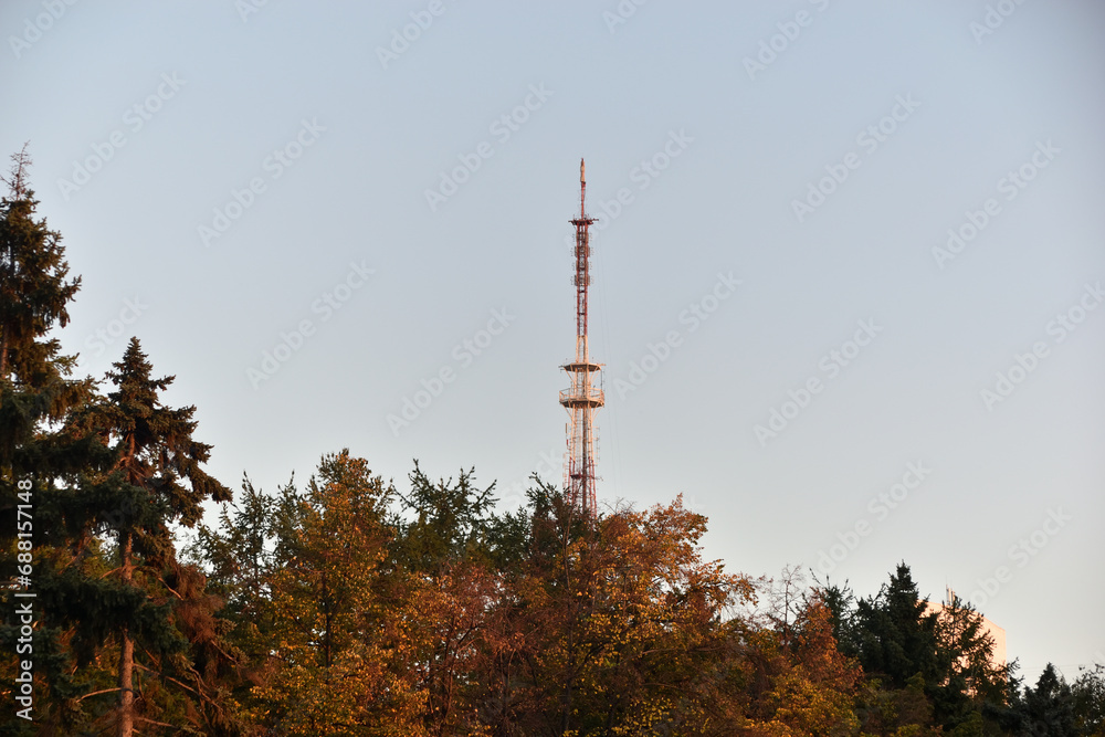 A television tower on the background of autumn trees. An iron high structure in the city. A television tower on the background of autumn trees. An iron high structure in the city.