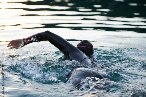 Triathlon athlete swimming on lake in sunrise wearing wetsuit © .shock