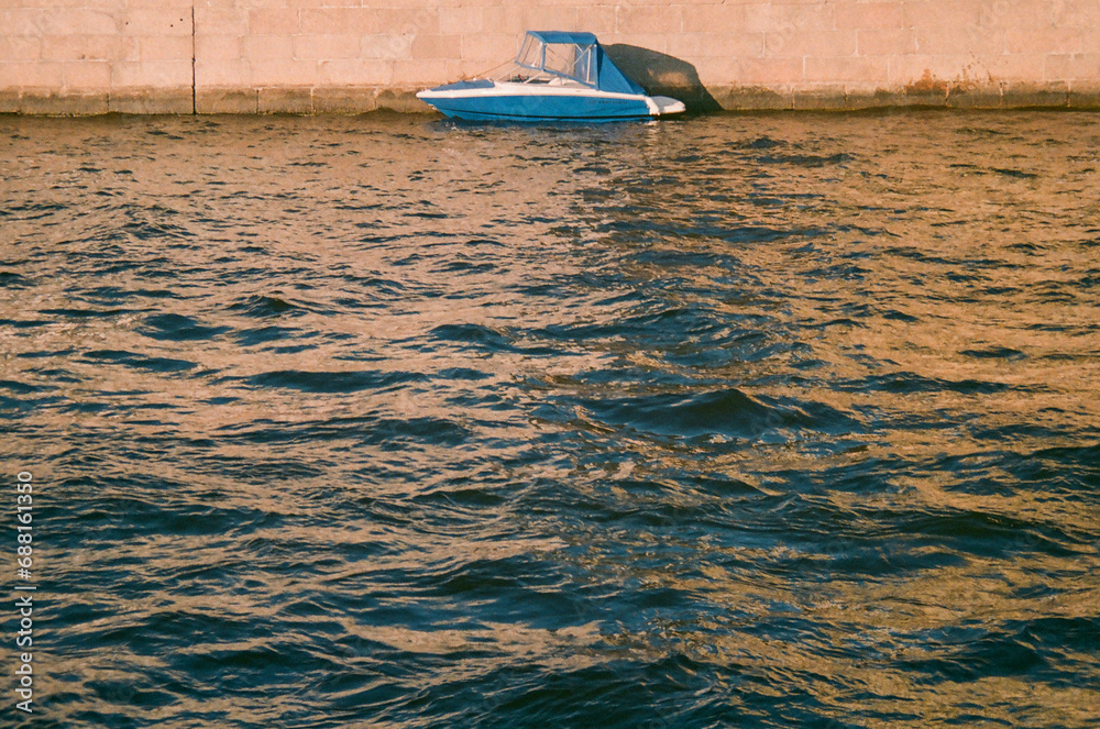 Obraz premium A blue boat reflected in the waves at sunset - film photography