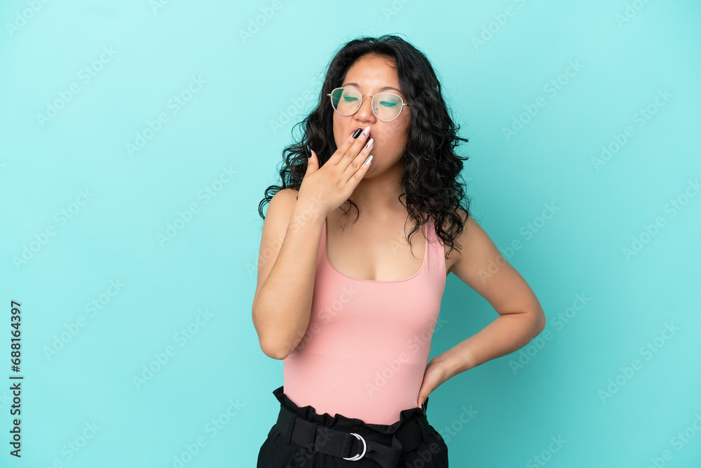 Young asian woman isolated on blue background yawning and covering wide open mouth with hand Young asian woman isolated on blue background yawning and covering wide open mouth with hand