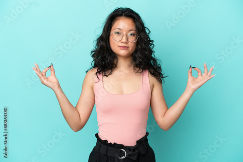 Young asian woman isolated on blue background in zen pose