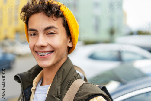 Portrait attractive smiling millennial boy wearing yellow hat, with dental braces on teeth looking at camera on urban street photo