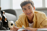 Portrait of attractive smiling boy with dental braces studying, learning language, taking notes lying on floor looking at camera. Education concept