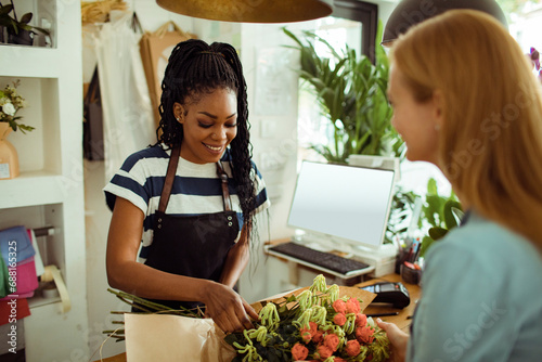 Female florist standing behind counter in plant store selling fresh flowers to client photo