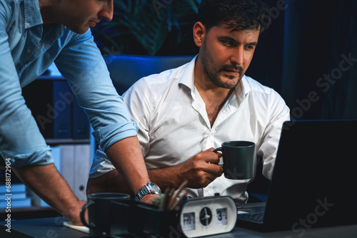 Supporting business partners discussing database market's launch platform online on laptop, one of man holing coffee cup to drink while thinking new project to present marketing strategy. Sellable. photo