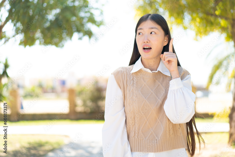 Pretty Chinese woman at outdoors thinking an idea pointing the finger up Pretty Chinese woman at outdoors thinking an idea pointing the finger up