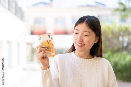 Pretty Chinese woman at outdoors taking a lot of money with happy expression