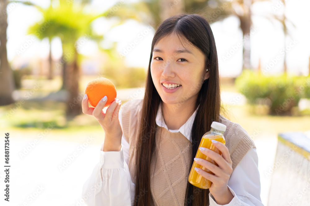 Pretty Chinese woman at outdoors holding an orange and an orange juice Pretty Chinese woman at outdoors holding an orange and an orange juice