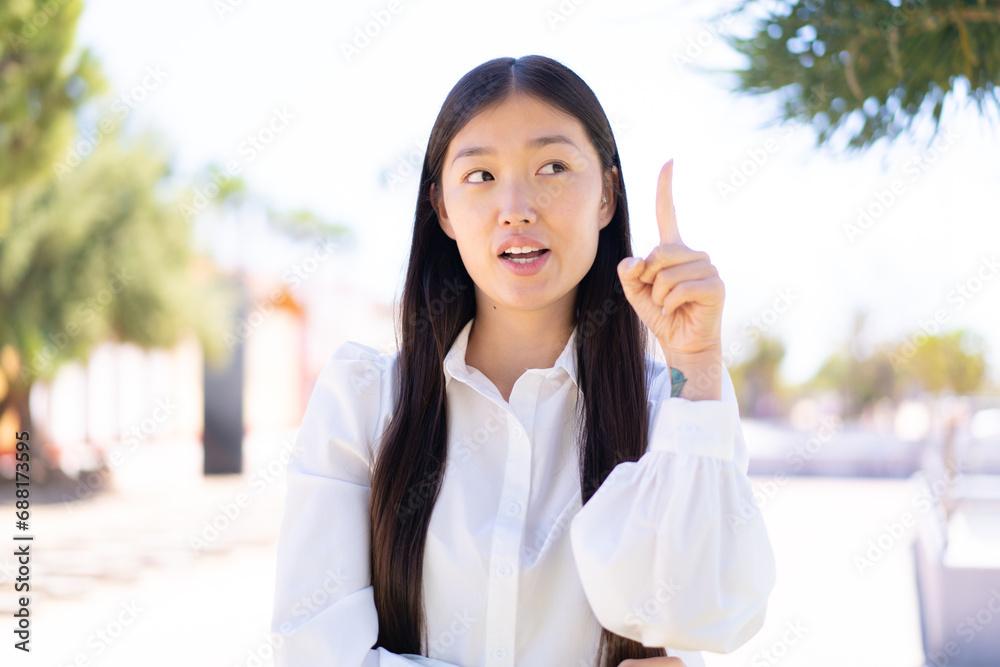 Pretty Chinese woman at outdoors thinking an idea pointing the finger up Pretty Chinese woman at outdoors thinking an idea pointing the finger up