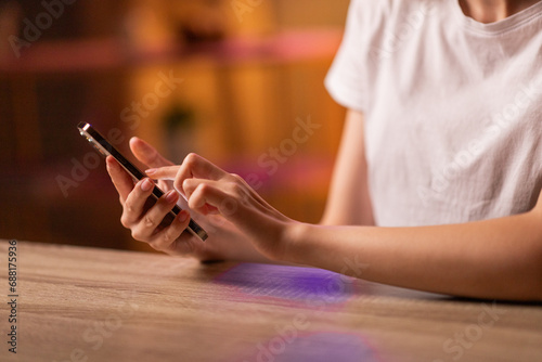 A girl or young woman sits at the table  holds in hands and uses a smartphone to correspond  read and send messages  watching video or spending leisure time on a social network. Close up. The