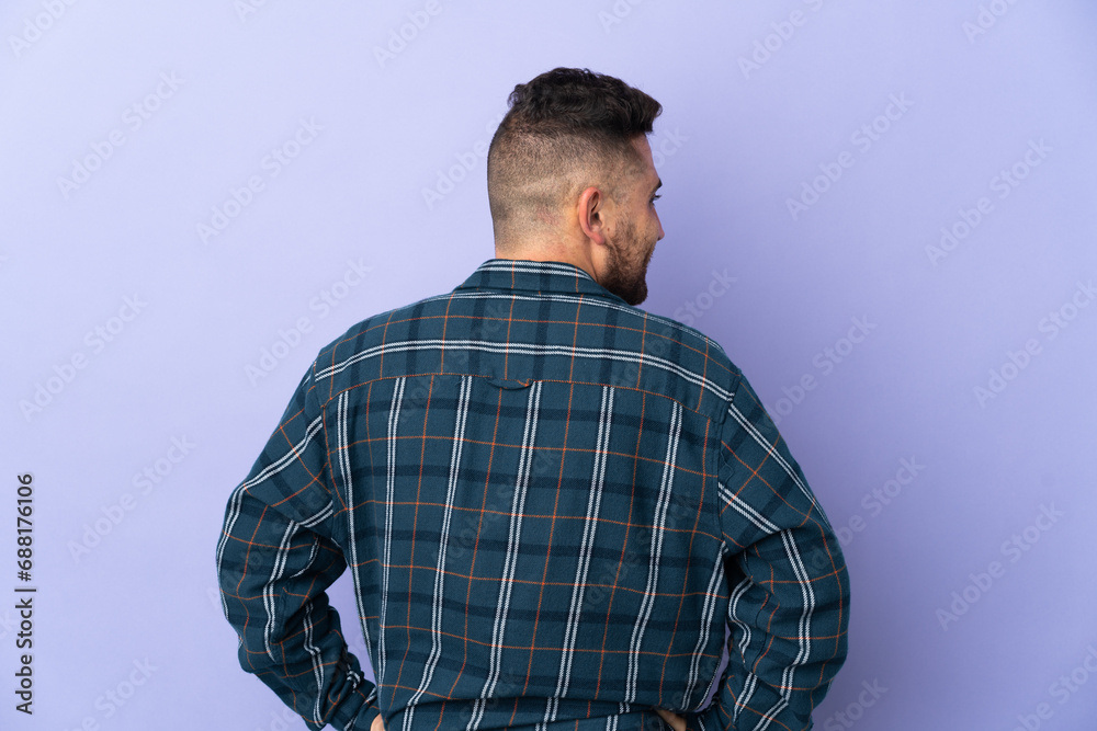 Caucasian man isolated on purple background in back position and looking side Caucasian man isolated on purple background in back position and looking side