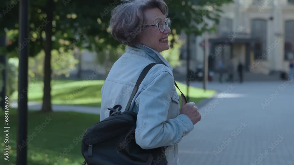 Retired positive woman with backpack traveling in city turning around to camera. Beautiful happy smiling grandmother in denim shirt turn back to see all perfectness urban architecture outdoors Retired positive woman with backpack traveling in city turning around to camera. Beautiful happy smiling grandmother in denim shirt turn back to see all perfectness urban architecture outdoors