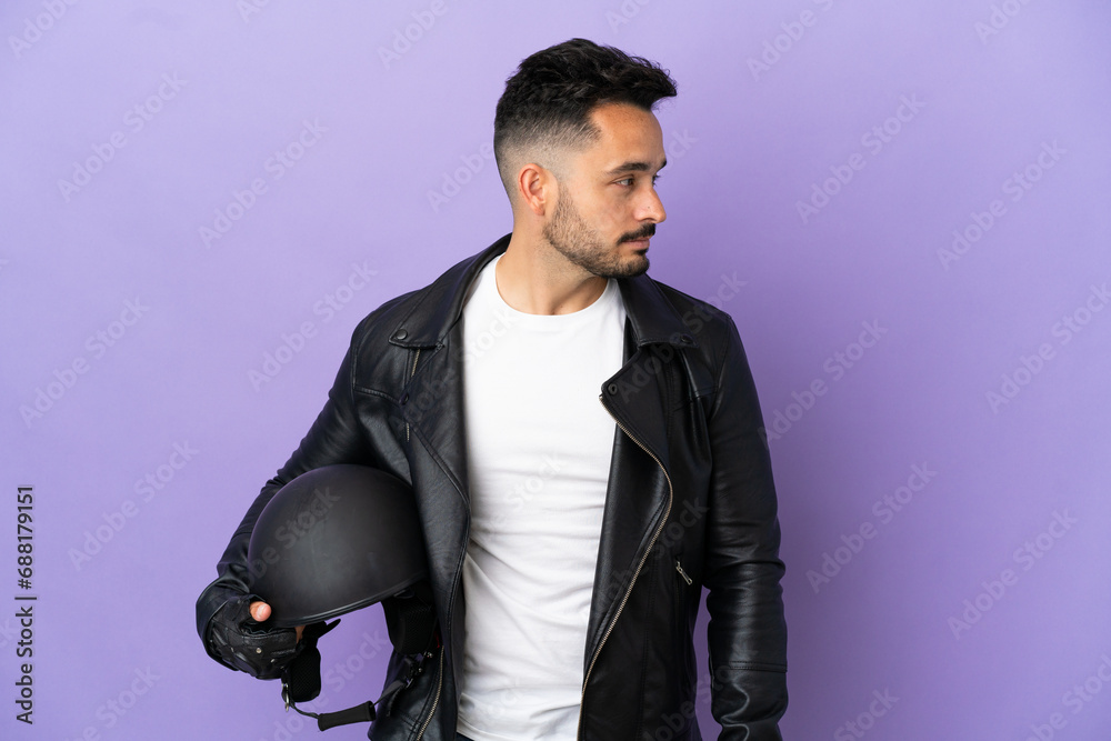 Young man with a motorcycle helmet isolated on purple background looking to the side Young man with a motorcycle helmet isolated on purple background looking to the side