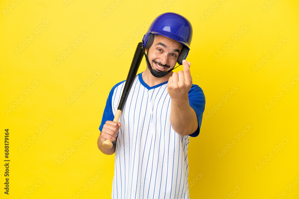 Young caucasian man playing baseball isolated on yellow background making money gesture