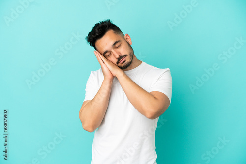 Young caucasian man isolated on blue background making sleep gesture in dorable expression