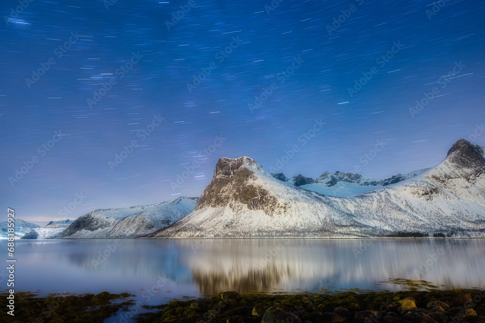 Mountains and starry night sky, Senja islands, Norway. Reflection on the water surface. Winter landscape with night sky. Norway travel image