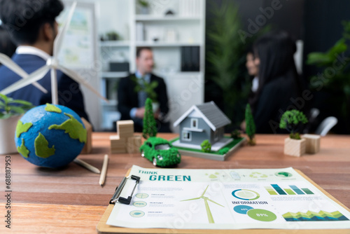 Mockup electric car with eco-friendly energy infrastructure on table with blurred background of productive business team meeting to contribute natural preservation and sustainable future. Quaint