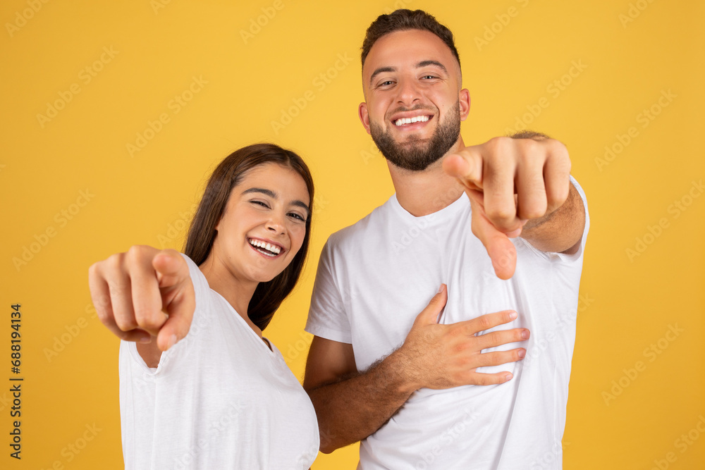 Smiling confident young european man and lady in white t-shirts point finger at camera Smiling confident young european man and lady in white t-shirts point finger at camera