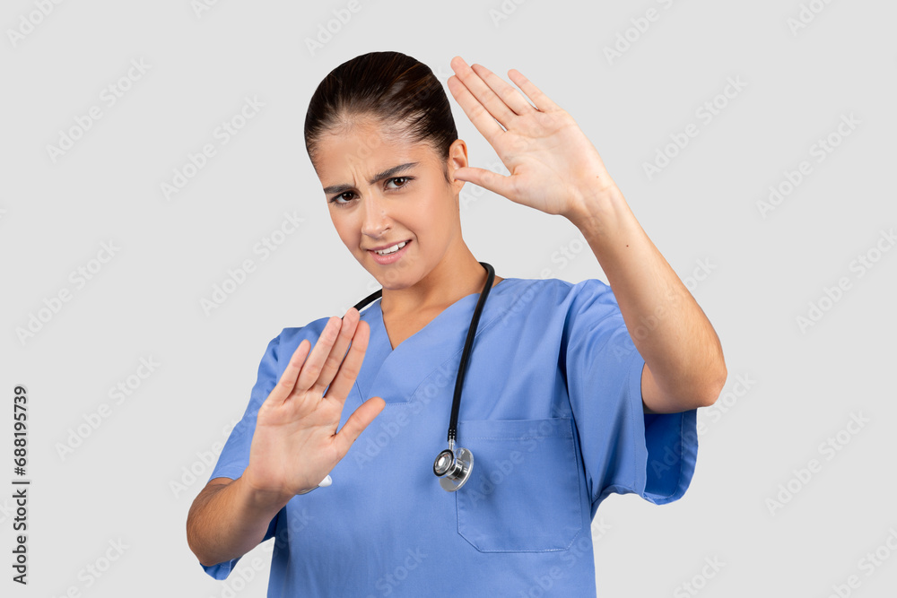 Unhappy european young doctor, nurse in blue uniform make stop gesture, keeping hands to defend Unhappy european young doctor, nurse in blue uniform make stop gesture, keeping hands to defend
