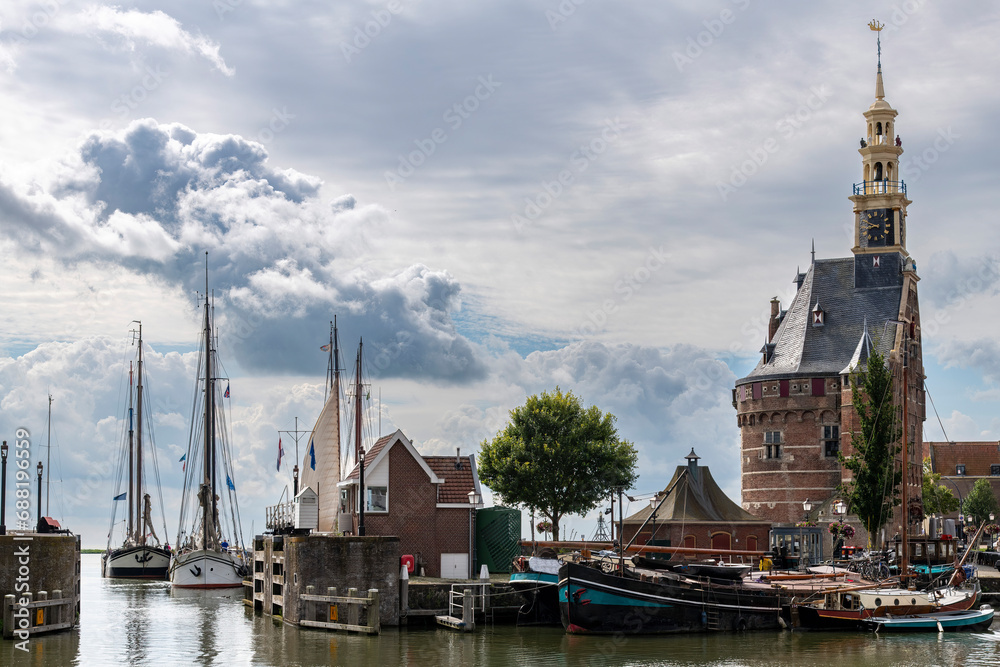 Panoramic view over inner harbor of Hoorn in the Netherlands towards outer harbor with traditional boats, historic buildings, main defense tower against a dramatic sky over the water